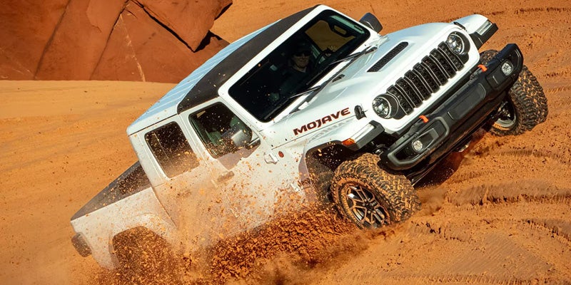 White Jeep Gladiator Mojave driving through desert sand with off-road capability.