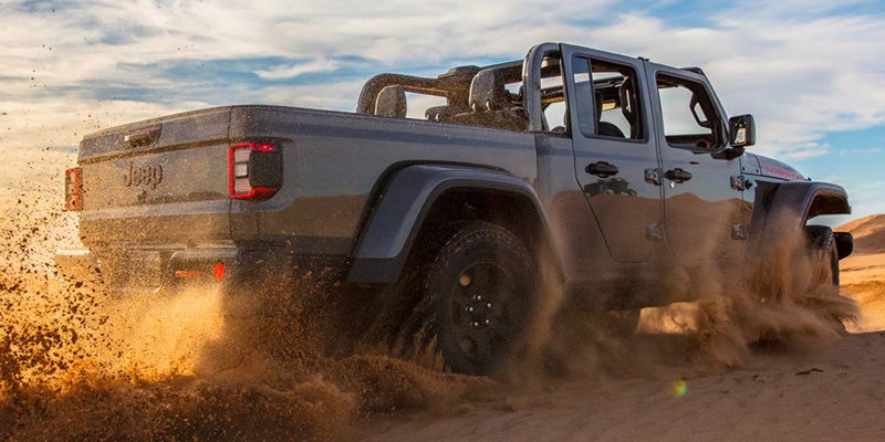 Gray Jeep Gladiator driving through muddy terrain with open-air styling.