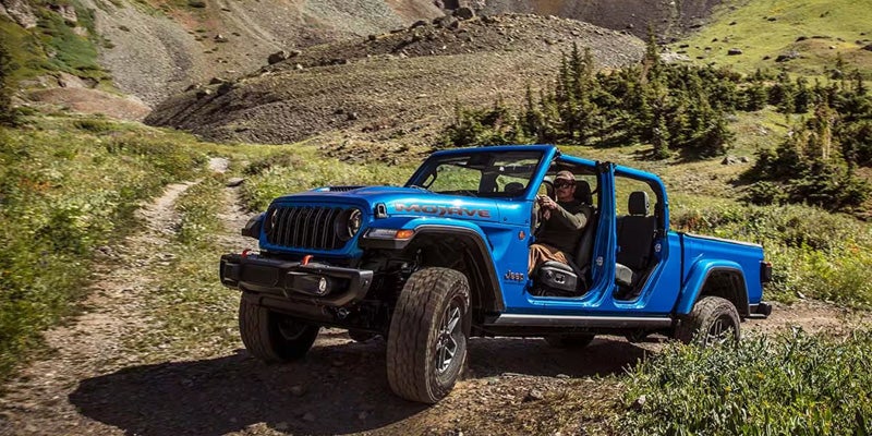 Blue Jeep Gladiator driving on a rugged mountain trail with doors removed.