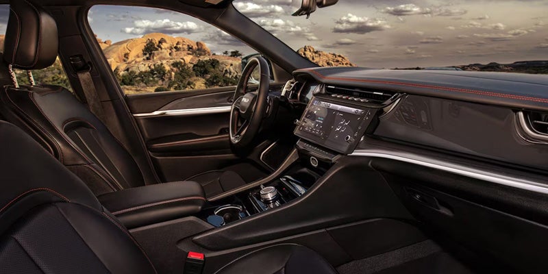 Jeep Grand Cherokee interior with premium dashboard, touchscreen display, and panoramic scenic view.