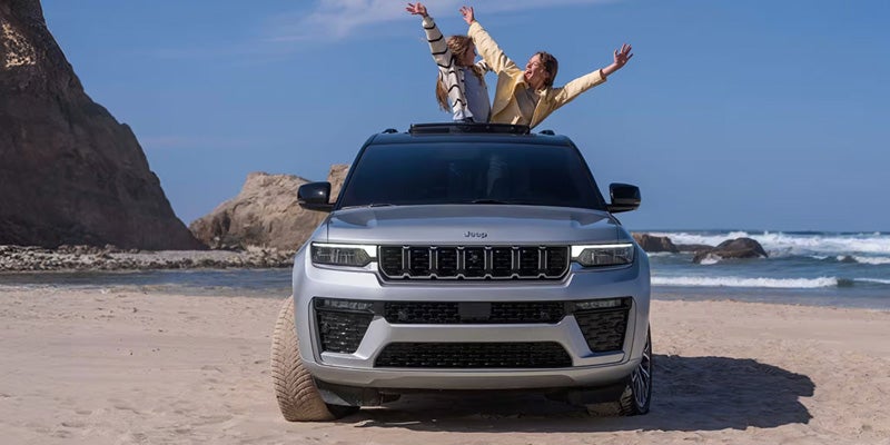 Jeep Grand Cherokee parked on a beach with passengers enjoying an outdoor adventure.