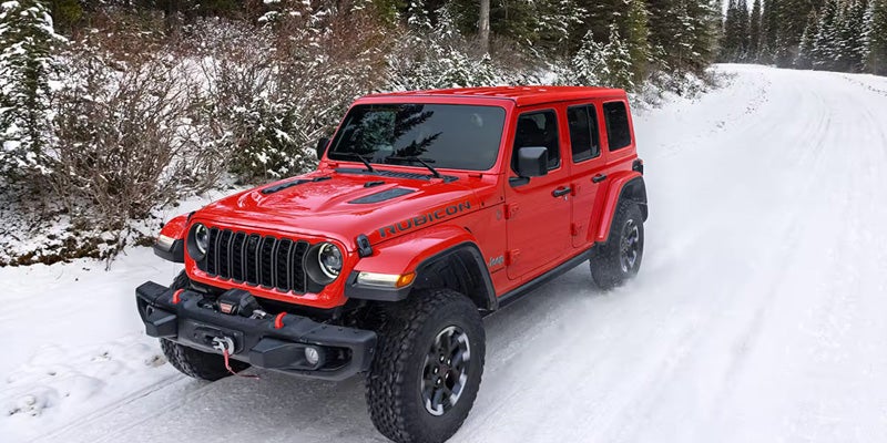 2026 Jeep Wrangler Rubicon red SUV driving through snowy trail