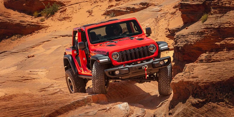2026 Jeep Wrangler Rubicon red SUV climbing rocky desert trail