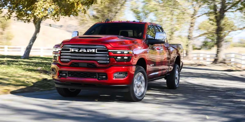Red Ram 2500 pickup truck driving on a tree-lined road.