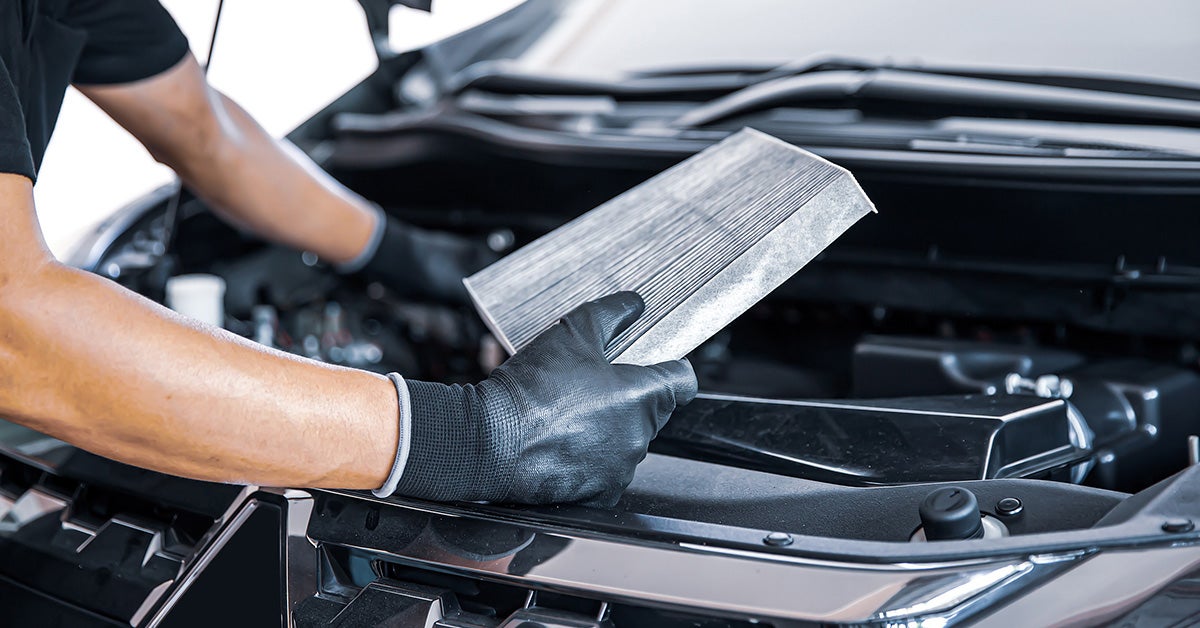 Auto technician at Jerry V Dodge replacing an engine air filter on a vehicle to maintain peak performance and protect the engine.