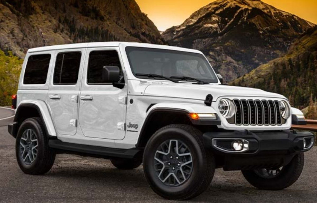 A white Jeep Wrangler SUV parked on a mountain road at sunset, with rugged peaks and trees in the background and a vivid orange sky overhead.