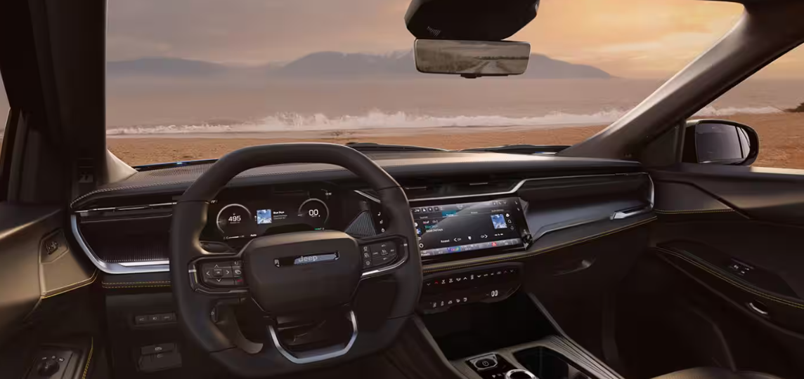 Interior of a 226 Jeep Cherokee with a digital display and steering wheel, overlooking a beach at sunset, for Windward Dodge Chrysler Jeep RAM.