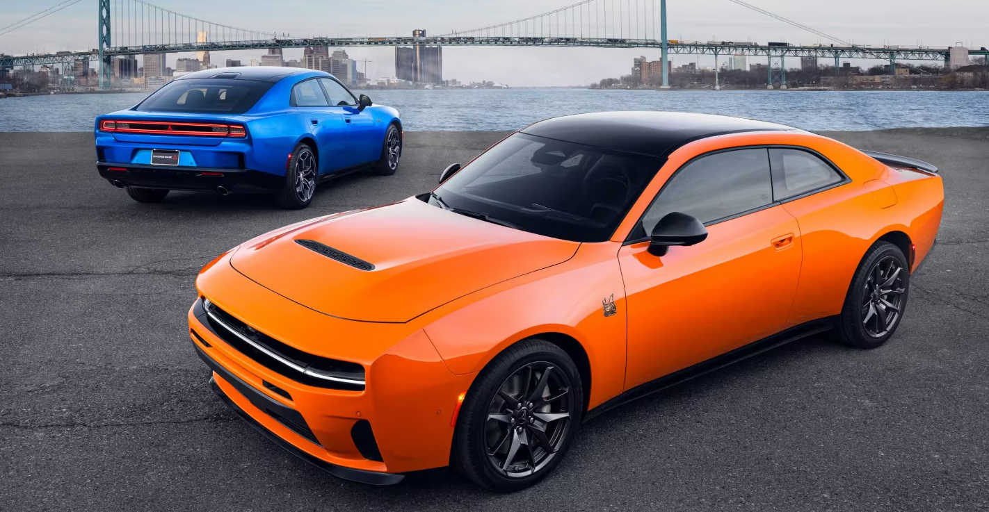 2026 Dodge Charger models parked near the water, including an orange coupe and a blue sedan.