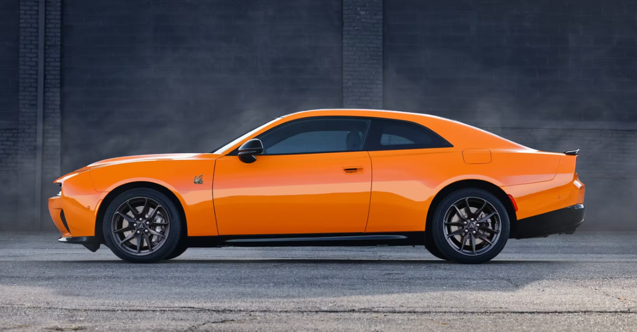 Side view of an orange 2026 Dodge Charger parked in an industrial setting.